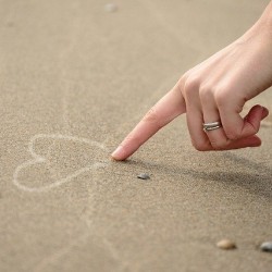 Hand malt Herz in den Sand